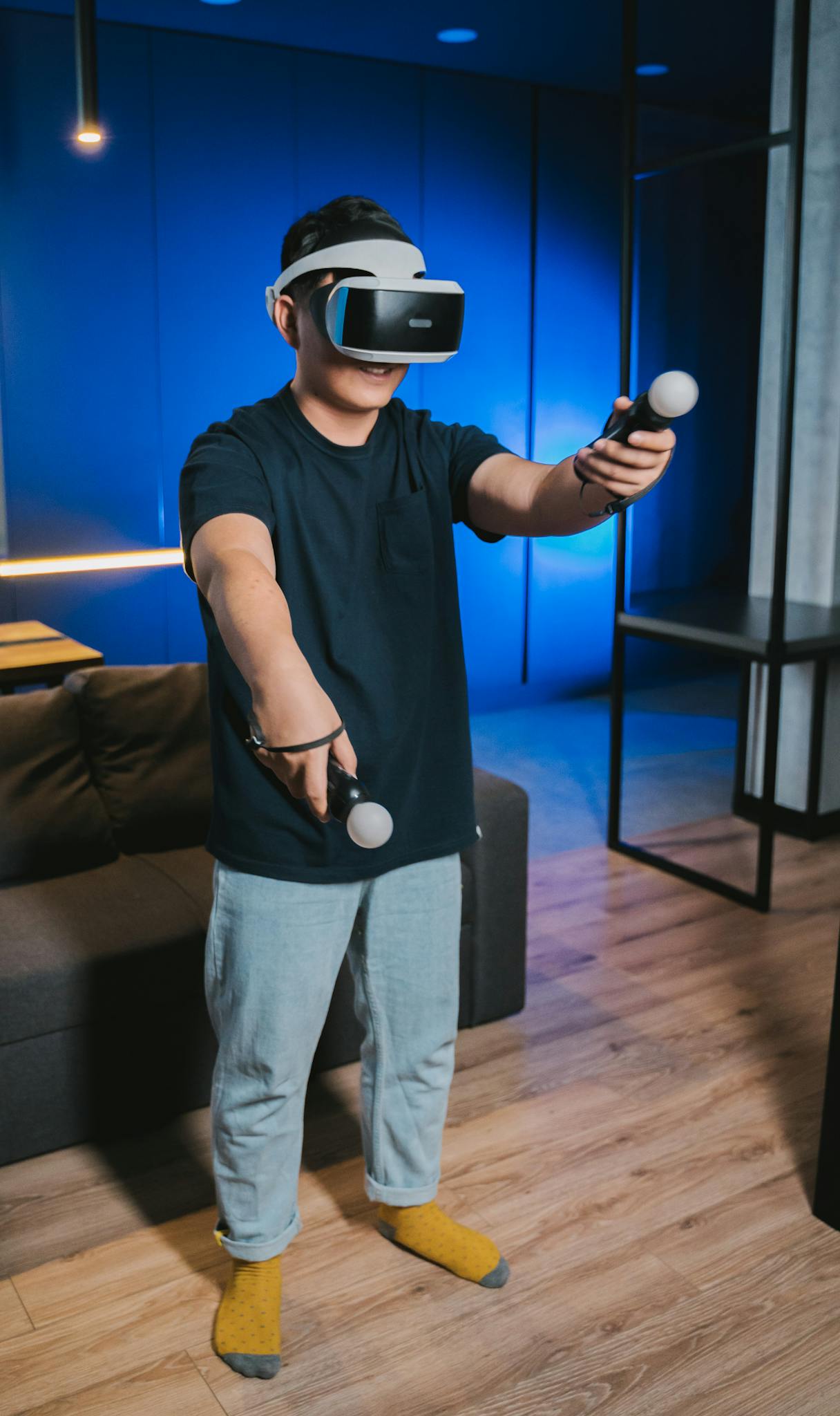 Man playing virtual reality game with VR goggles and controllers indoors.
